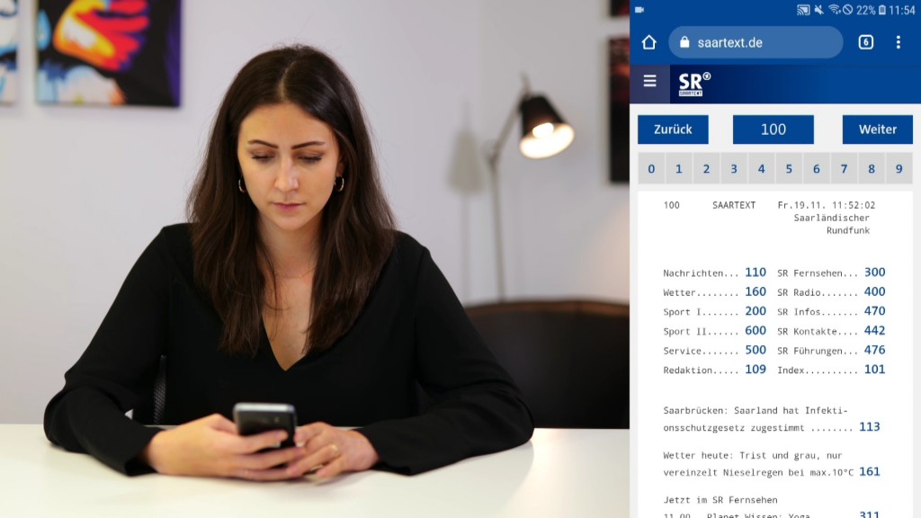 Foto: Eine Frau sitzt mit einem Handy in der Hand am Tisch