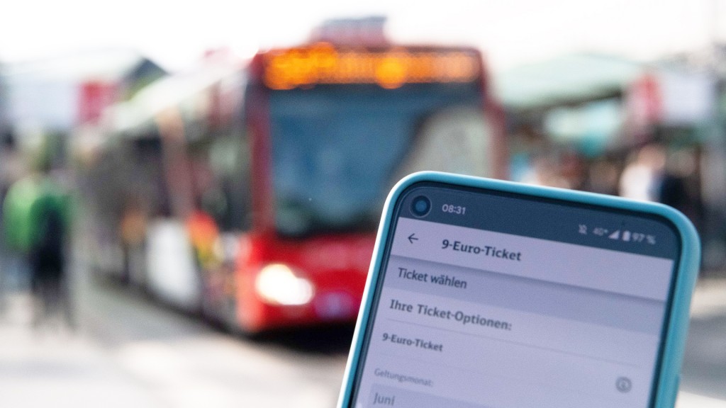 Auf einem Handy ist die Buchungsseite des 9-Euro-Tickets aufgerufen mit einem roten Bus im Hintergrund.