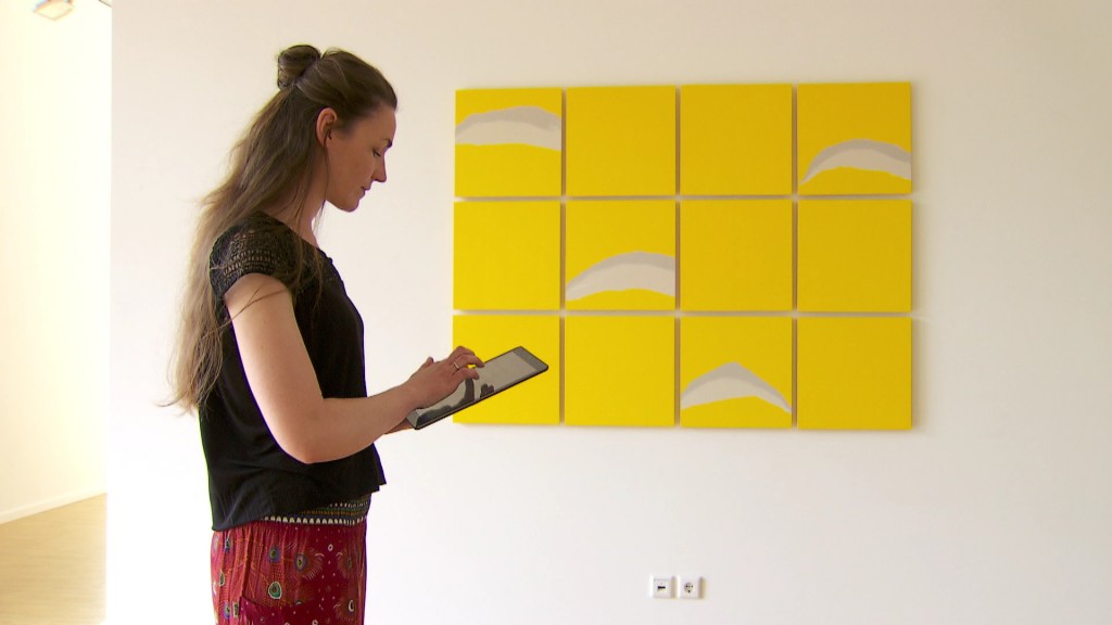 Foto: Eine Frau steht mit einem Tablet vor einem Kunstwerk
