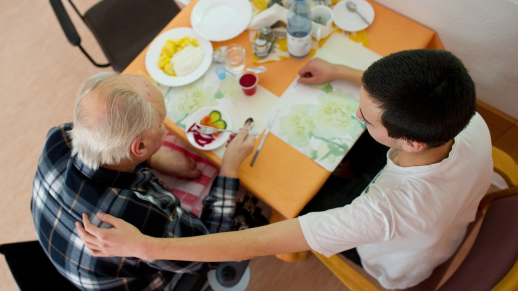 Junger Mann hilft einer Heimbewohnerin beim Einnehmen der Mahlzeit