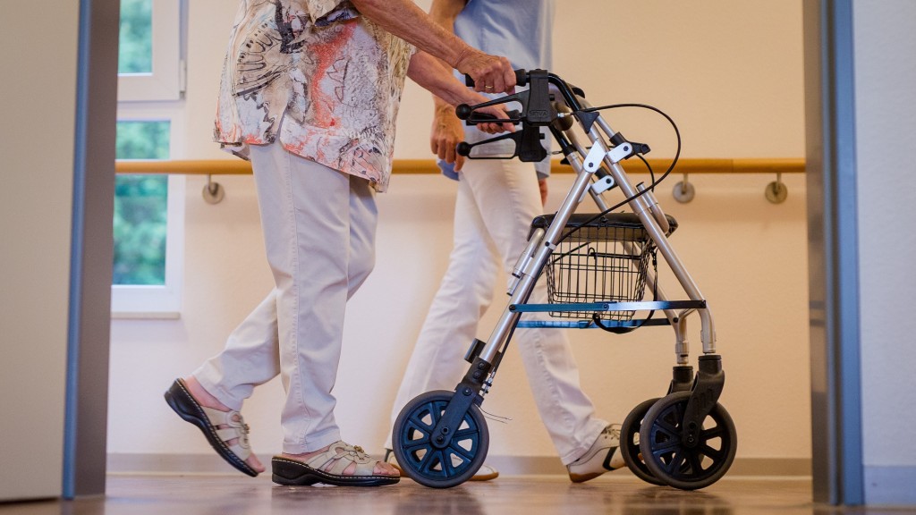Foto: Eine Pflegekraft geht in einem Pflegeheim mit einer älteren Dame über einen Korridor