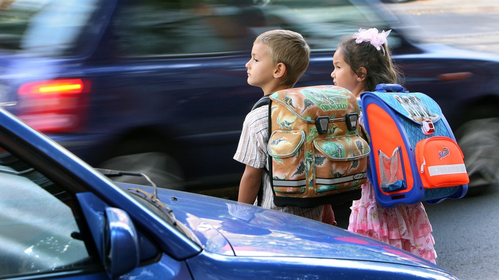 Schulkinder überqueren zwischen geparkten Autos die Straße