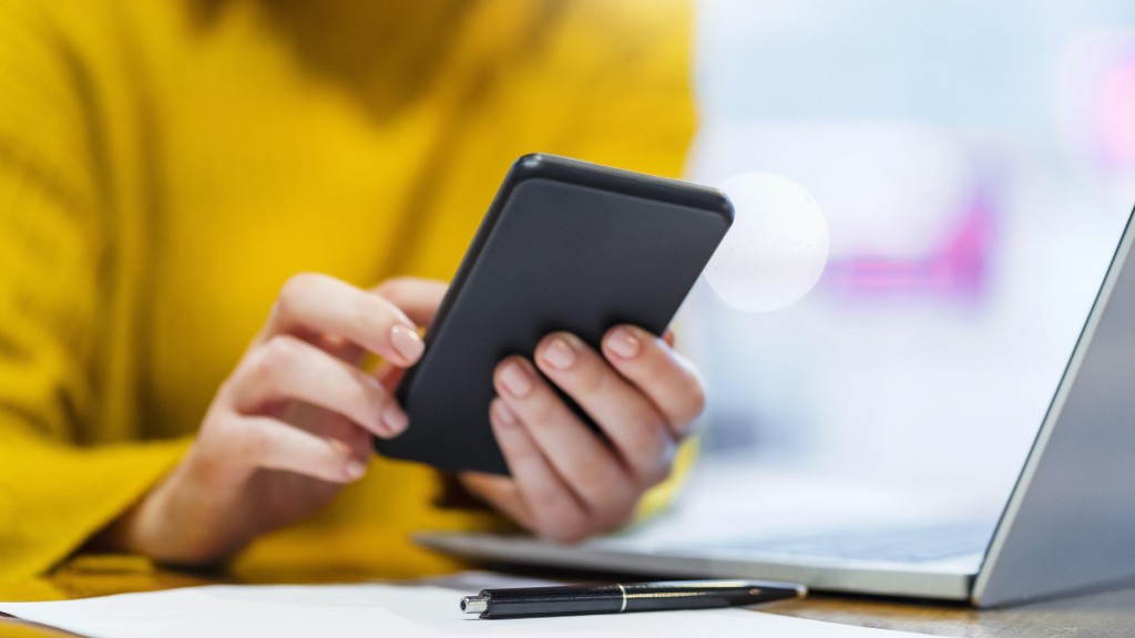 Frau sitzt mit Handy am Laptop