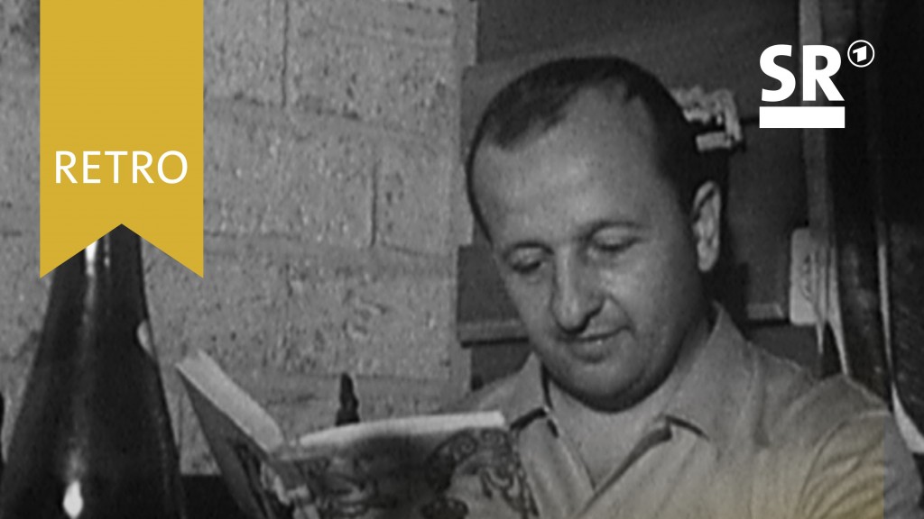 Ein Mann liest ein Buch, auf dem Tisch steht eine Weinflasche und ein Weinglas