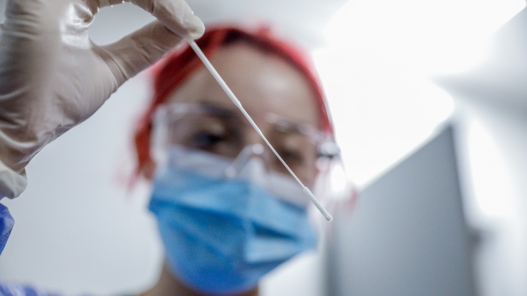Foto: Eine Mitarbeiterin in einer Klinik führt einen Covid-19 - Test durch und hält ein Teststäbchen für den Abstrich vor sich. 