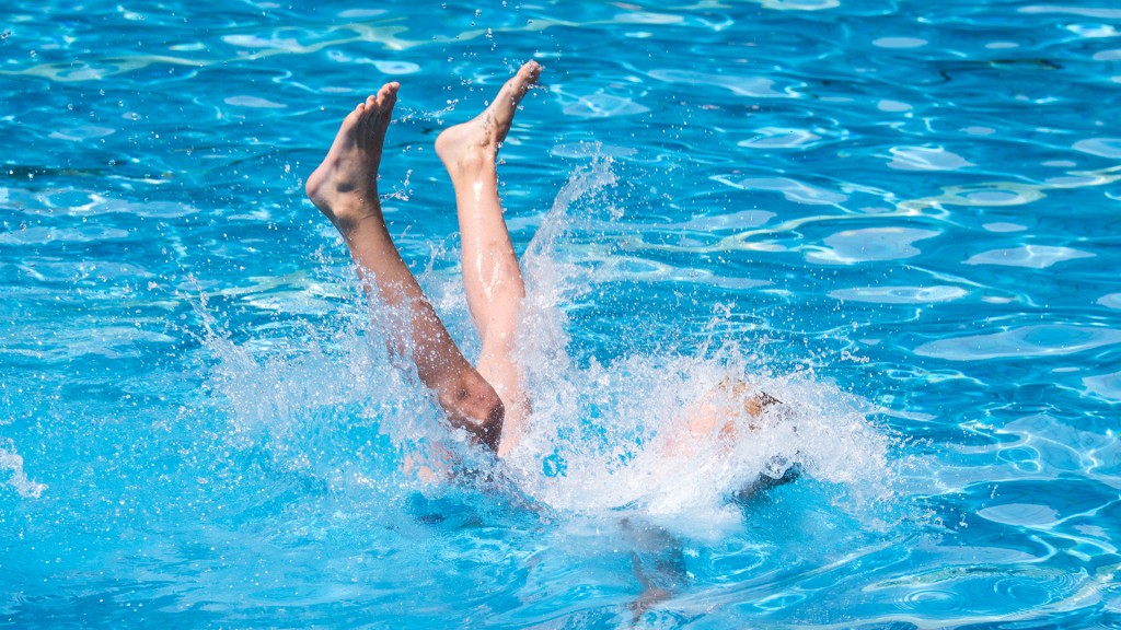 Ein Junge wird in einem Freibad ins Wasser geworfen.