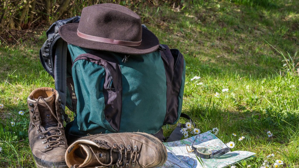 Eine Wanderausrüstung - Rucksack, Landkarte, Kompass, Wanderschuhen und Hut - liegt auf einer Wiese