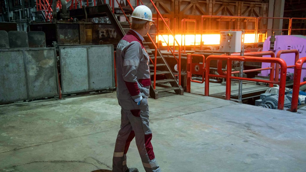 Foto: Ein Stahlarbeiter der Stahlproduktion beobachtet eine glühende Bramme, die aus dem Ofen auf die Walzstrasse bewegt wird