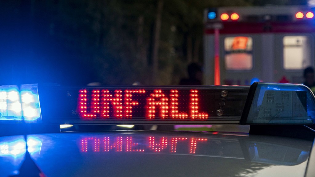 Foto: Ein Einsatzfahrzeug der Polizei mit Blaulicht und dem Schriftzug Unfall im Display. Im Hintergrund ein Rettungswagen.