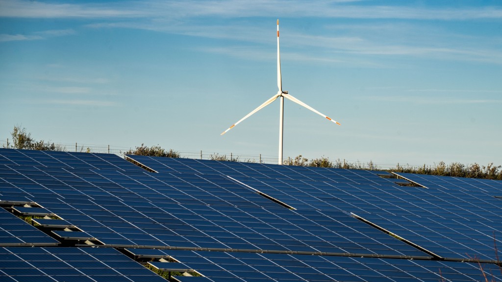 Eine großflächige Solaranlage steht auf einem Feld, im Hintergrund steht ein Windrad auf einem Hügel