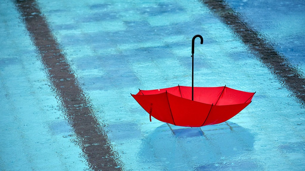 Bei strömendem Regen schwimmt ein Regenschirm im Freibad in einem Becken