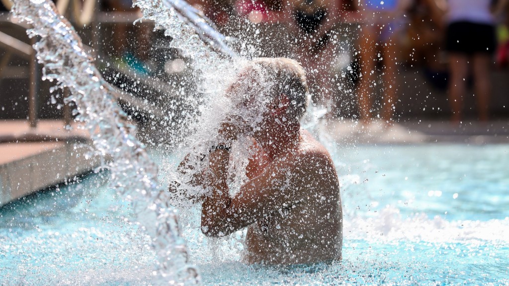 Foto: Ein Mann erfrischt sich in einem Freibad unter einer Wasserfontäne.