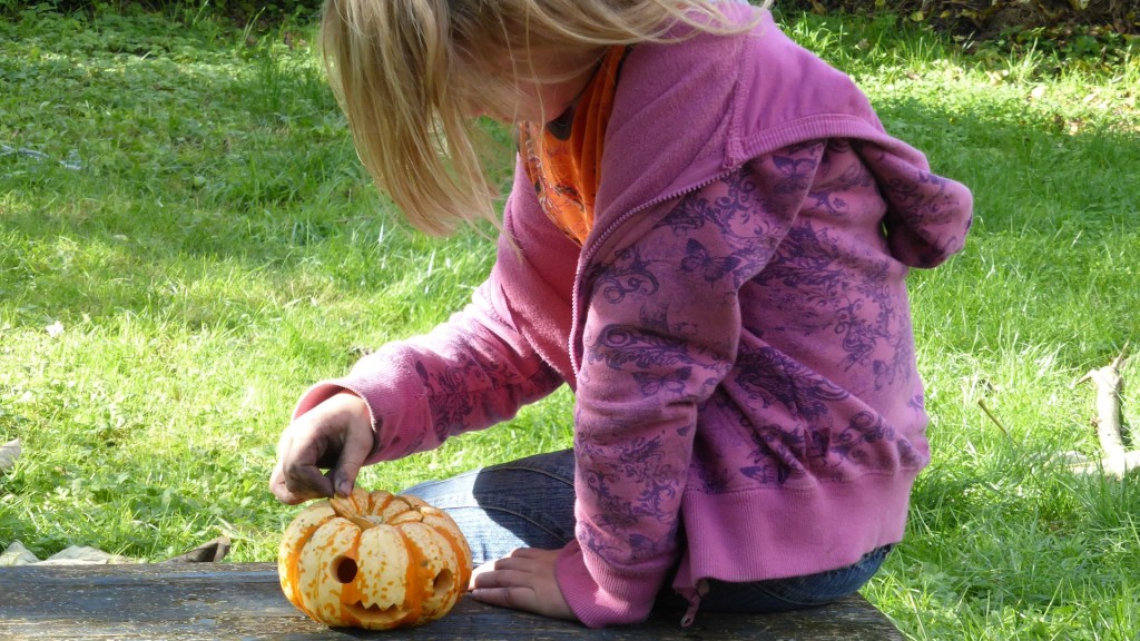 Mädchen sitzt auf einer Bank und bastelt einen Halloween-Kürbis