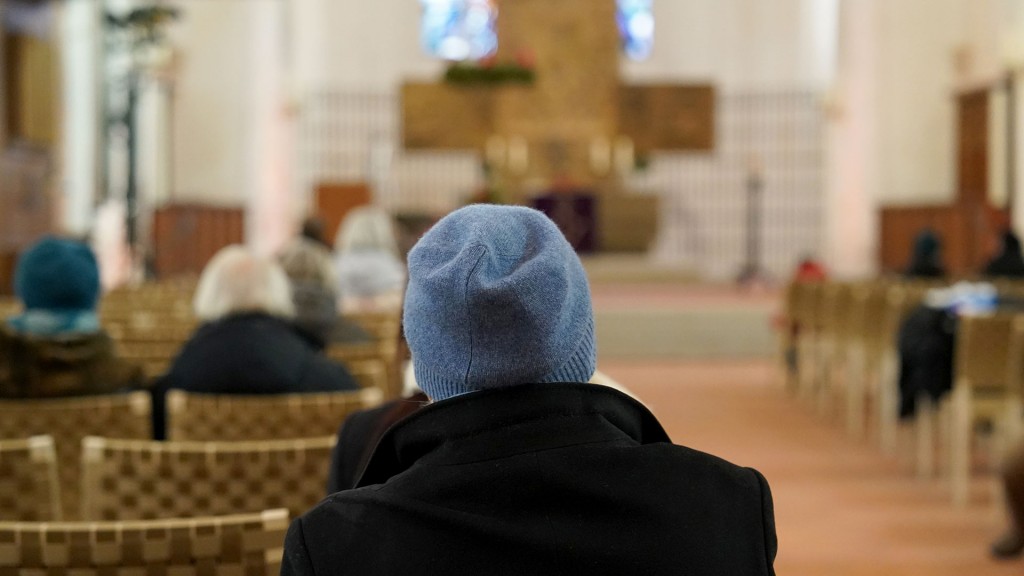 Besucher einer Kirche sitzen mit Jacken und Mützen in den Bänken