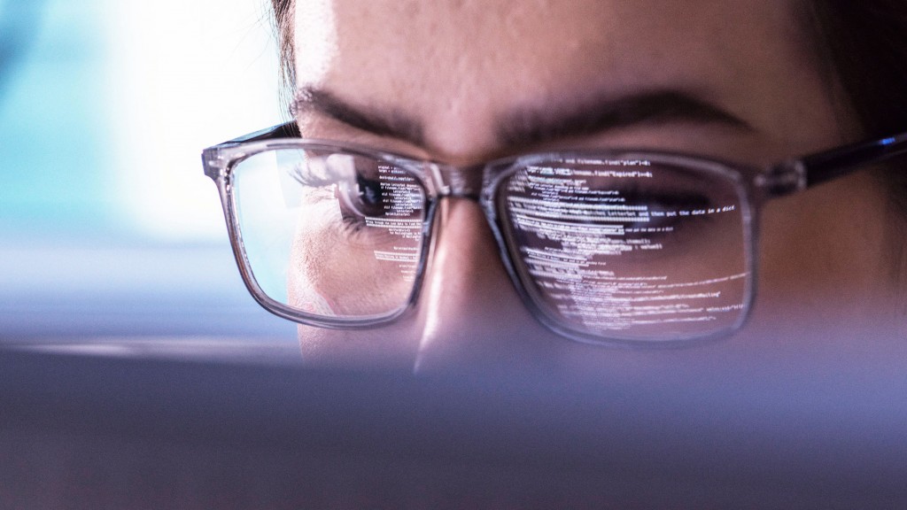 Foto: In der Brille einer Person in Nahaufnahme speigeln sich Code-Zeilen eines Computerbildschirms