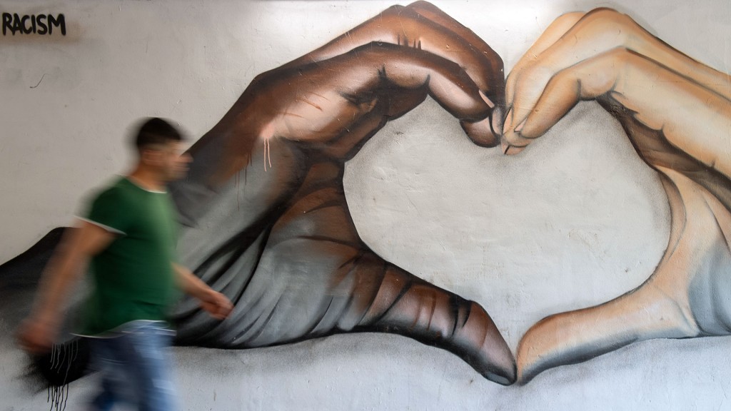 Foto: Ein Mann geht an einer Wand vorbei, auf die der Straßenkünstler Nath Murdoch eine dunkelhäutige und eine hellhäutige Hand gemalt hat, die zusammen ein Herz formen