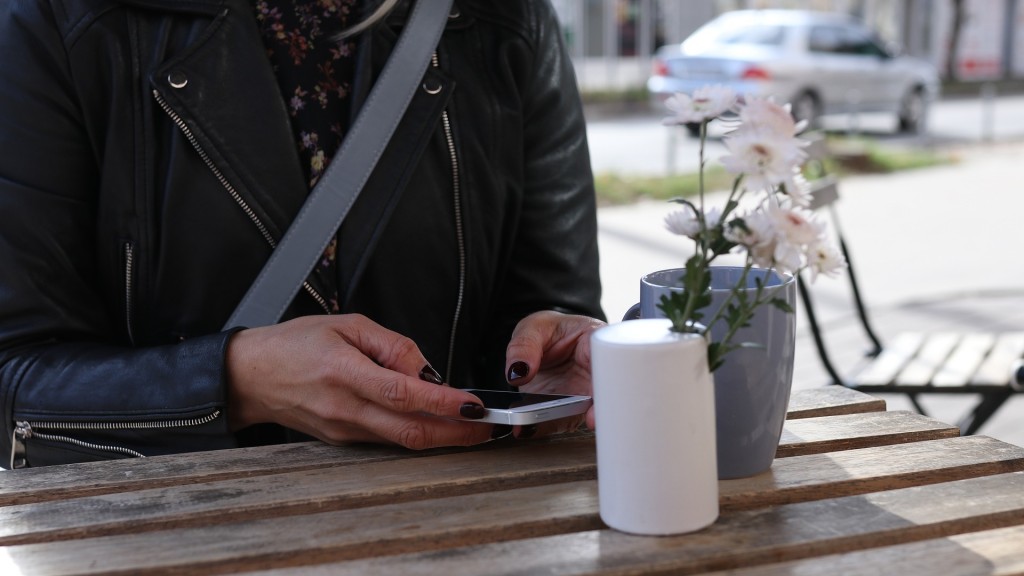 Eine Frau sitzt mit ihrem Handy draußen an einem Bistro Tisch.