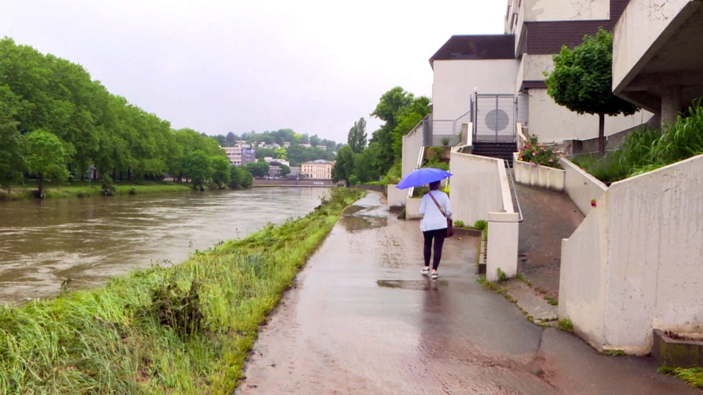 Der Pegel der Saar normalisiert sich nach dem Hochwasser, eine Frau mit Regenschirm auf dem vorher überfluteten Fußweg