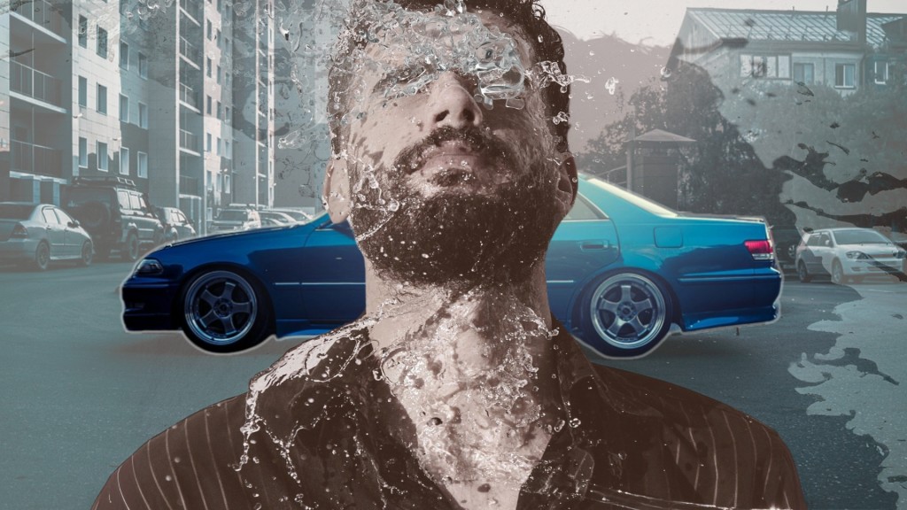 Ein Mann, dessen Gesicht von spritzendem Wasser verdeckt wird. Im Hintergrund sieht man ein glänzendes, blaues Auto. 