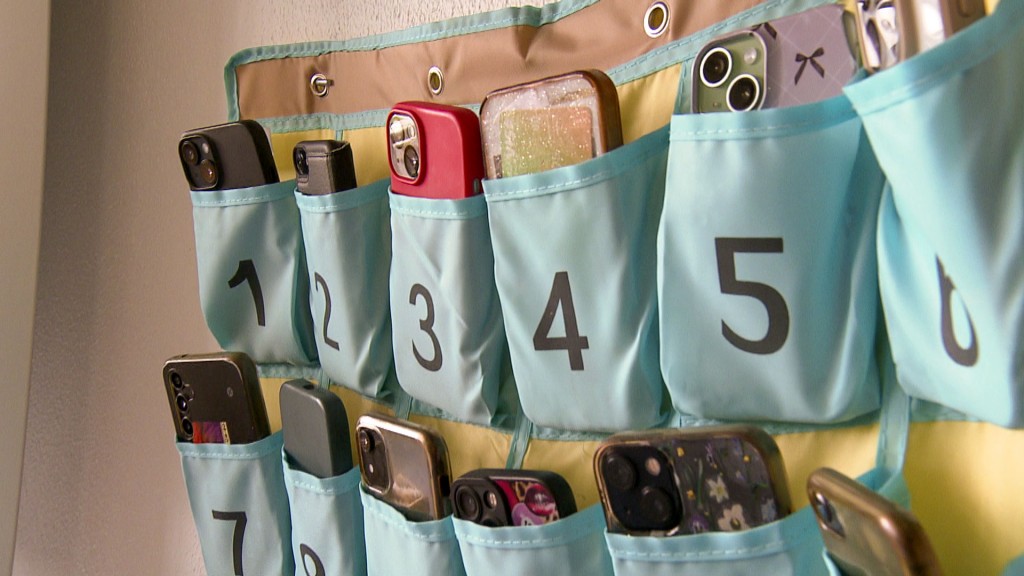Foto: Smartphones von Schülern hängen während des Unterrichts in Stoffsäckchen neben der Tafel