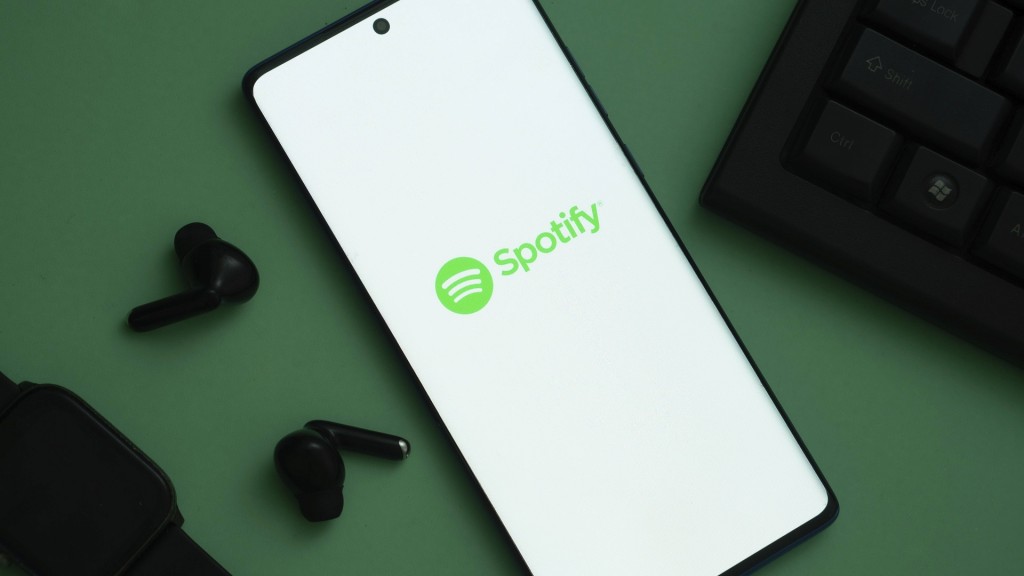 Spotify Logo auf dem Handy-Bildschirm mit schwarzen Ohrhörern daneben auf grünem Hintergrund 