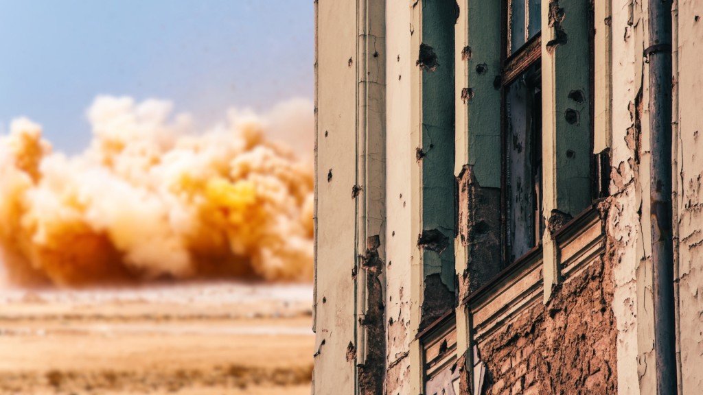 Das Bild oben zeigt ein zerstörtes, zerbombtes Gebäude und im Hintergrund eine Wolke von einer Explosion.