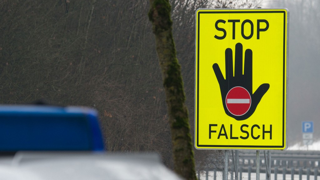Ein Hinweisschild mit der Aufschrift „Stop Falsch“ steht hinter einem Polizeifahrzeug an einer Autobahn