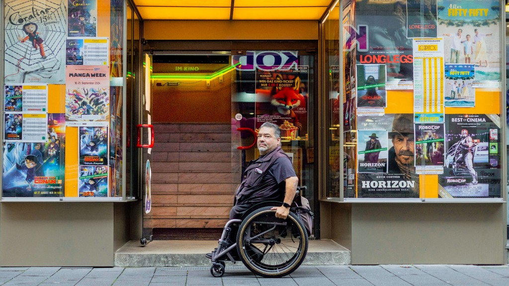 Ein Rollstuhlfahrer steht vor dem Treppenaufgang eines Kinos