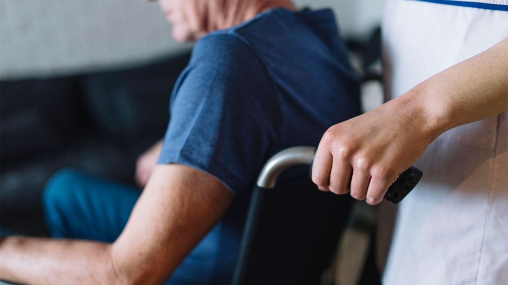 Alter Mann in einem Rollstuhl, der von einer Pflegekraft geschoben wird