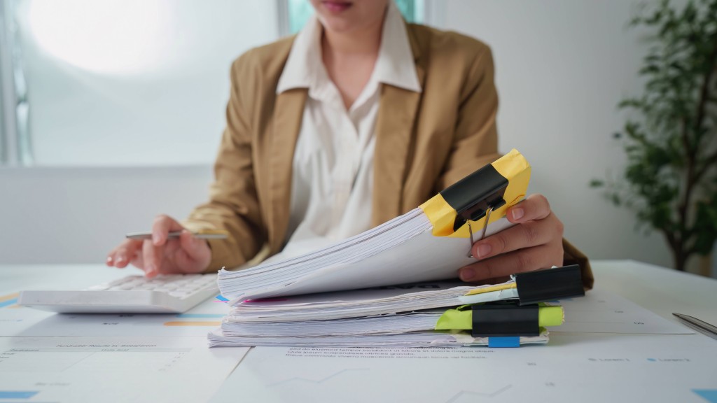 Frau bearbeitet einen Papierstapel am Schreibtisch.