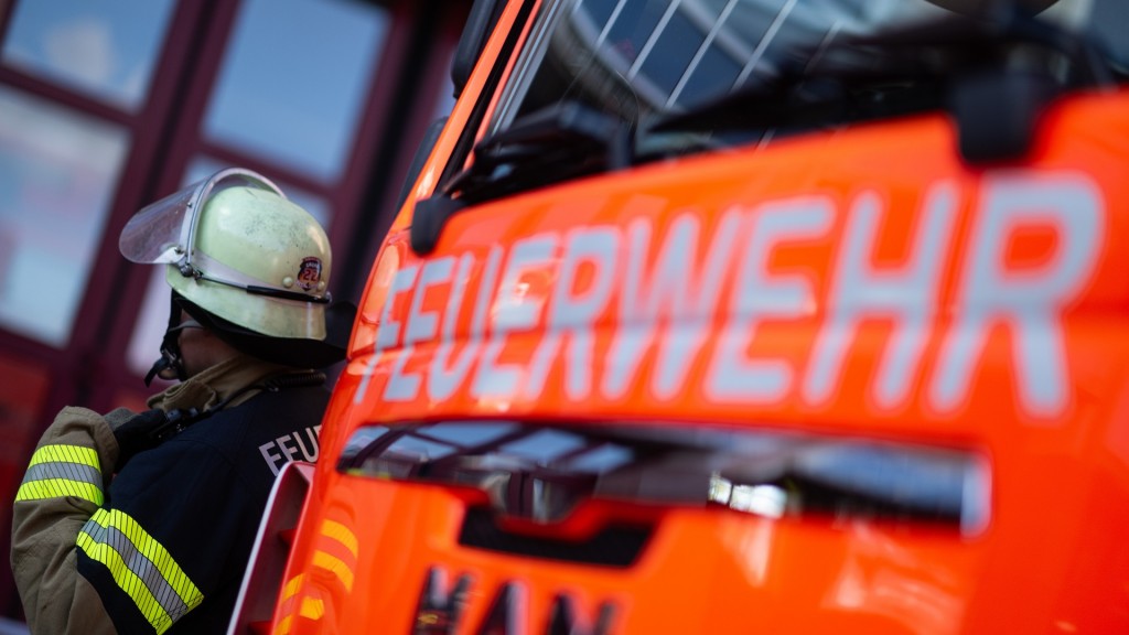 Eine Einsatzkraft der Feuerwehr steht neben einem Einsatzfahrzeug der Feuerwehr. 