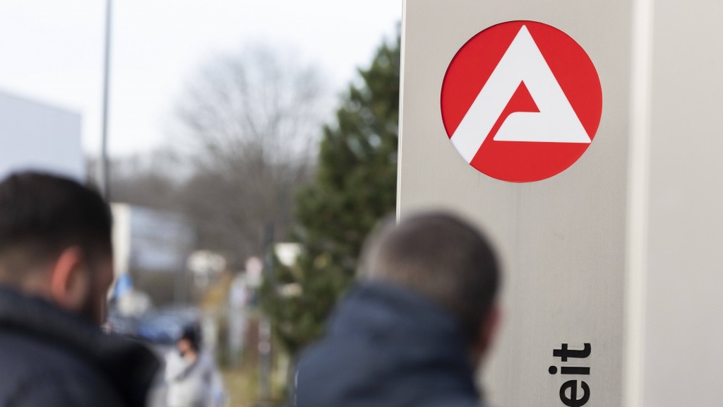 Stele mit dem Zeichen, Logo der Agentur für Arbeit vor dem Gebäude. Personen unscharf im Vordergrund