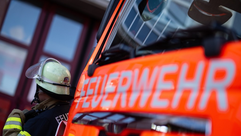 Eine Einsatzkraft der Feuerwehr steht neben einem Einsatzfahrzeug der Feuerwehr. 