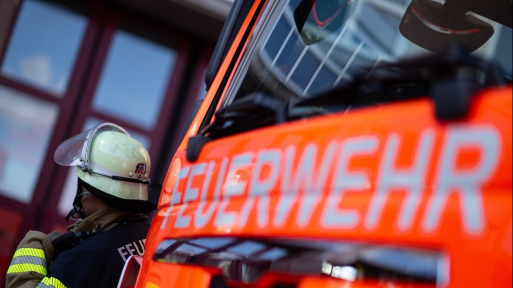 Foto: Eine Einsatzkraft der Feuerwehr steht neben einem Einsatzfahrzeug der Feuerwehr. 