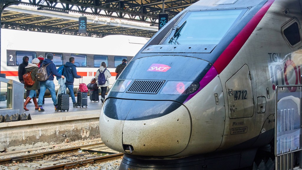 Foto: Reisende auf einem Bahnsteig. Im Vordergrund steht ein TGV der französischen Bahn.