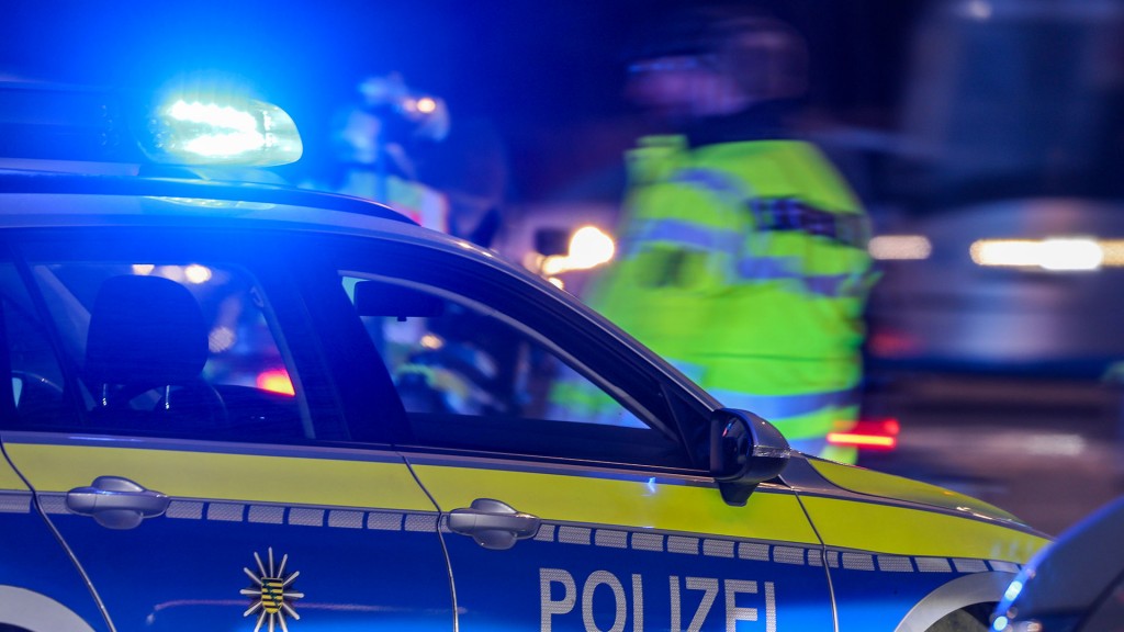 Foto: Ein Polizist steht am Abend neben seinem Polizeifahrzeug mit Blaulicht