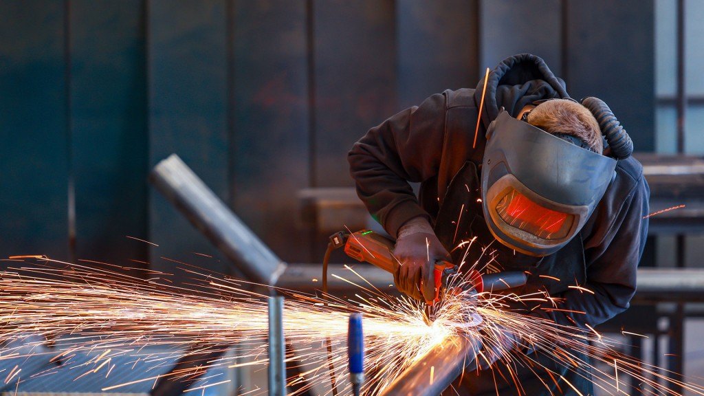 Foto: Ein Industriearbeiter flext mit einem Winkelschleifer ein Stahlrohr