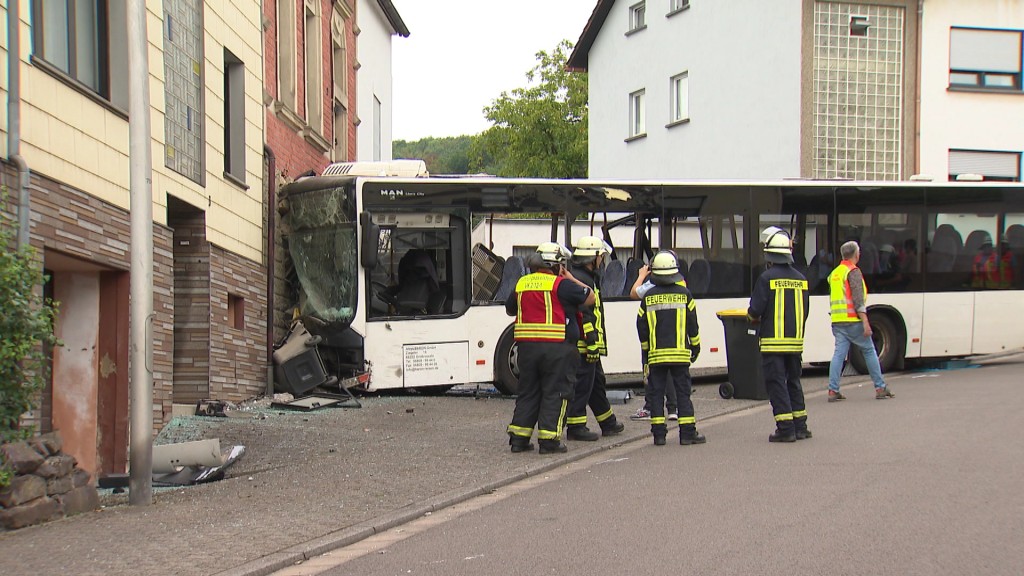 Foto: Eine Gruppe von Feuerwehrleuten steht vor dem beschädigten Bus