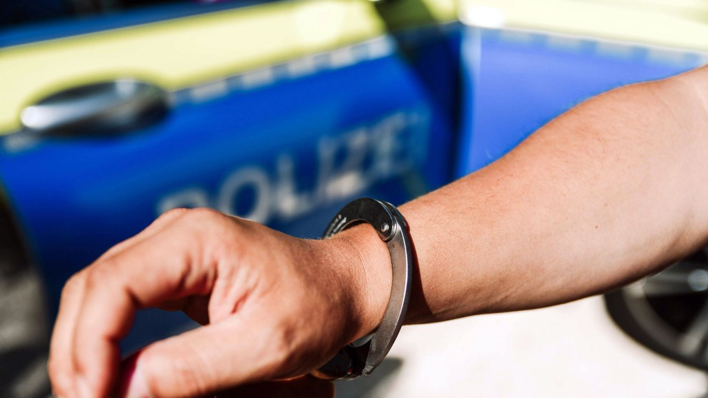 Symbolbild: Handschellen an einem Handgelenk vor einem Polizeiwagen