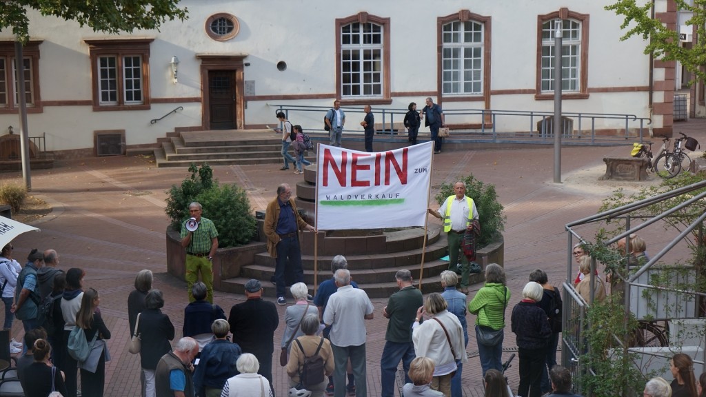 Foto: Menschen versammeln sich auf einem Platz mit einem Schild