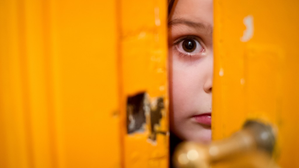 Ein junges Mädchen schaut verängstigt durch einen Türschlitz (Foto: dpa)
