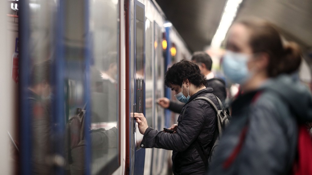 Fahrgäste mit Mund-Nasen-Bedeckung stehehn an einer Bahn