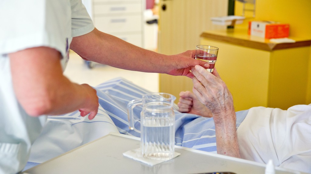 Krankenpflegerin reicht einer Patientin ein Glas Wasser