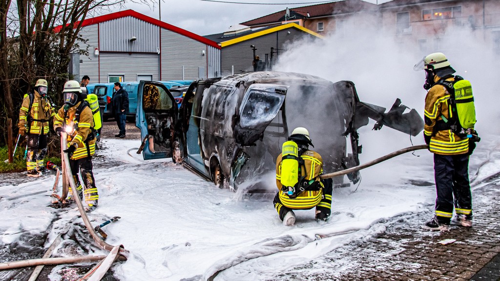 Foto: Feuerwehrleute stehen vor dem ausgebrannten Geldtransporter