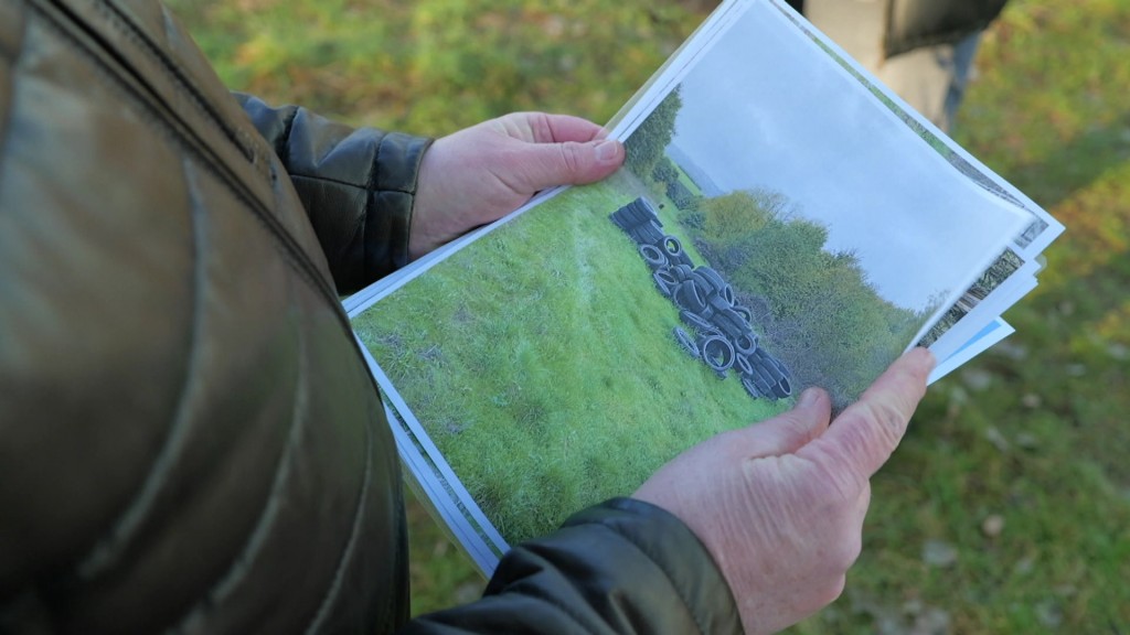 Foto: Ein Mann hält ein Bild von einem Reifenberg auf einem Feld in der Hand