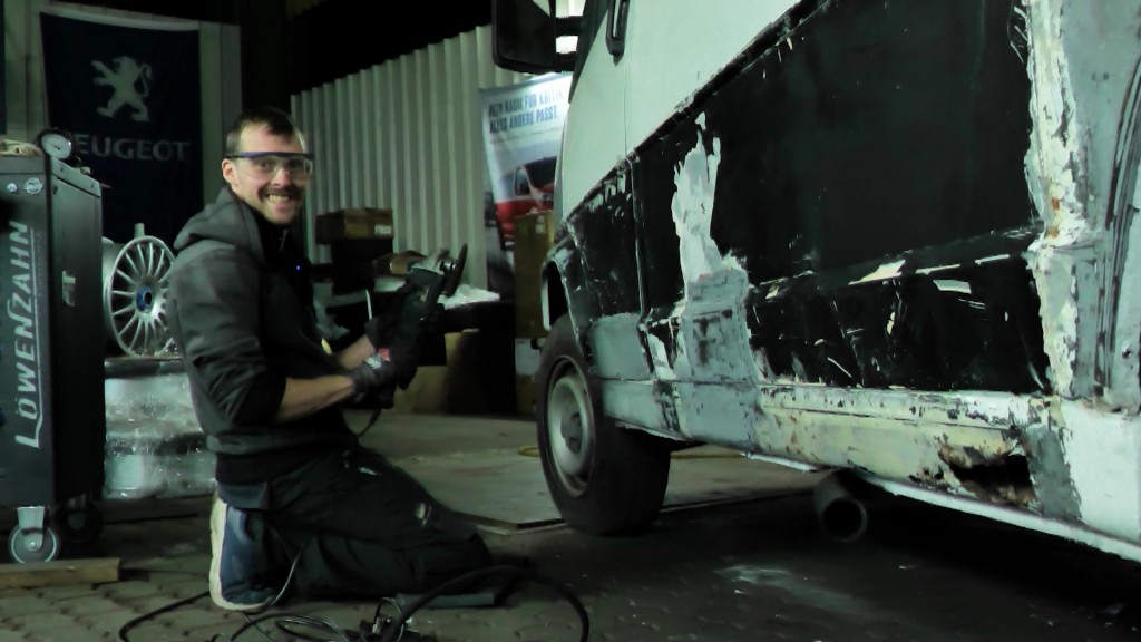 Foto: Ein am Auto schraubender Mann grinst in die Kamera.