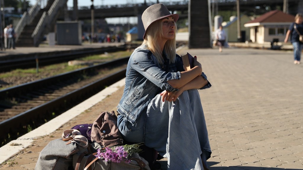 Frau sitzt mit Koffern auf einem Bahnsteig