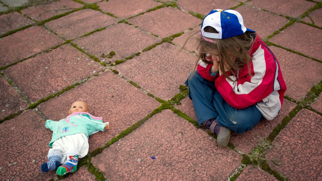 Ein Mädchen sitzt mit einer Puppe allein am Boden.