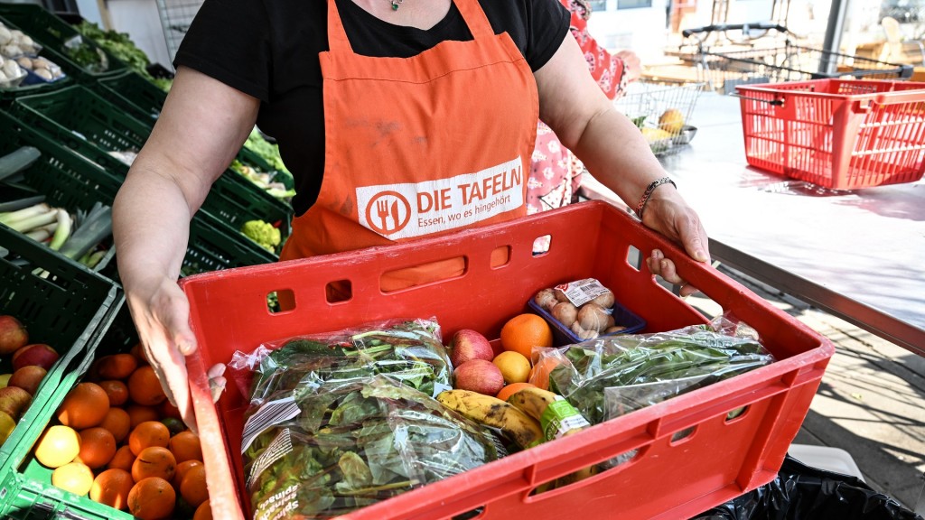Eine Mitarbeiterin des Tafel-Ladens trägt eine Kiste voll mit Obst und Gemüse.
