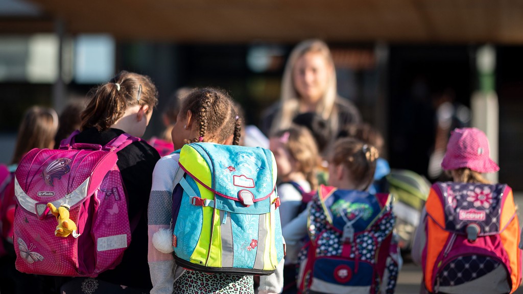 Kinder mit Schulranzen stehen vor einer Grundschule auf dem Hof